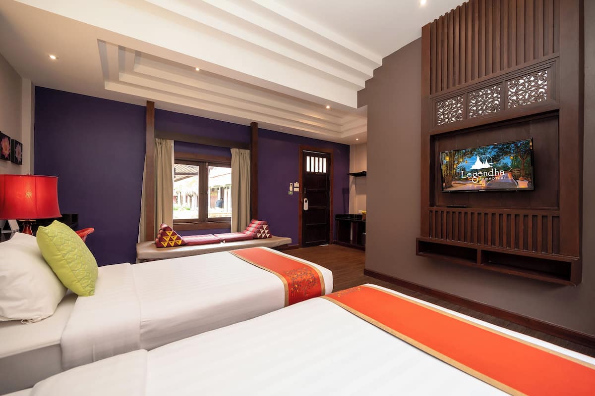 A hotel room with two beds, a TV mounted on the wall, and a window with curtains.