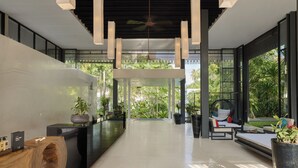 Un interior moderno con un espacio central abierto, mobiliario blanco y negro, y vistas a zonas verdes exteriores.