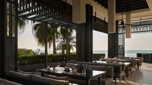 Un restaurante frente al mar con terraza, ventanas amplias y vistas al océano.