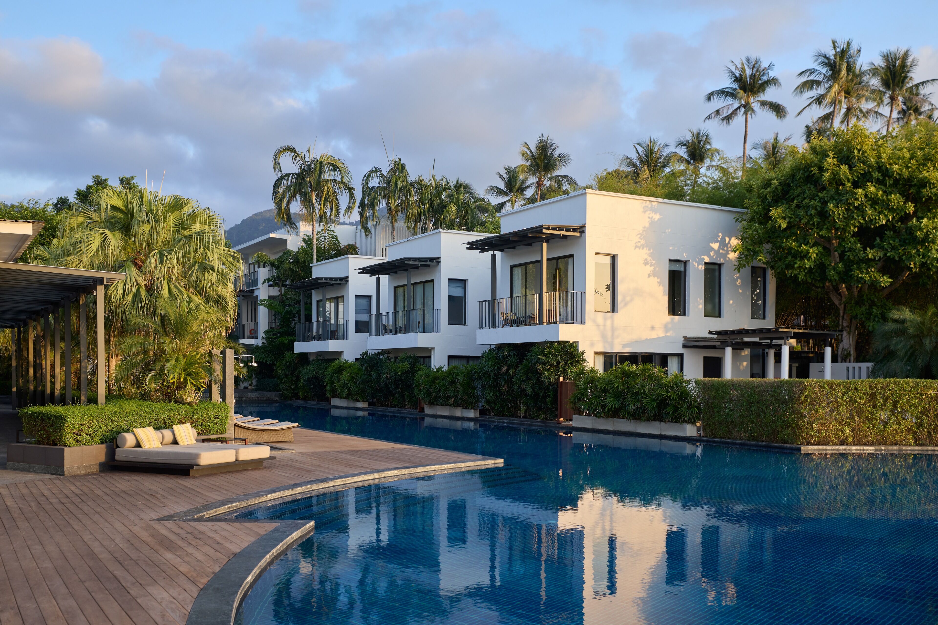 A modern resort with a swimming pool, white buildings, and palm trees.
