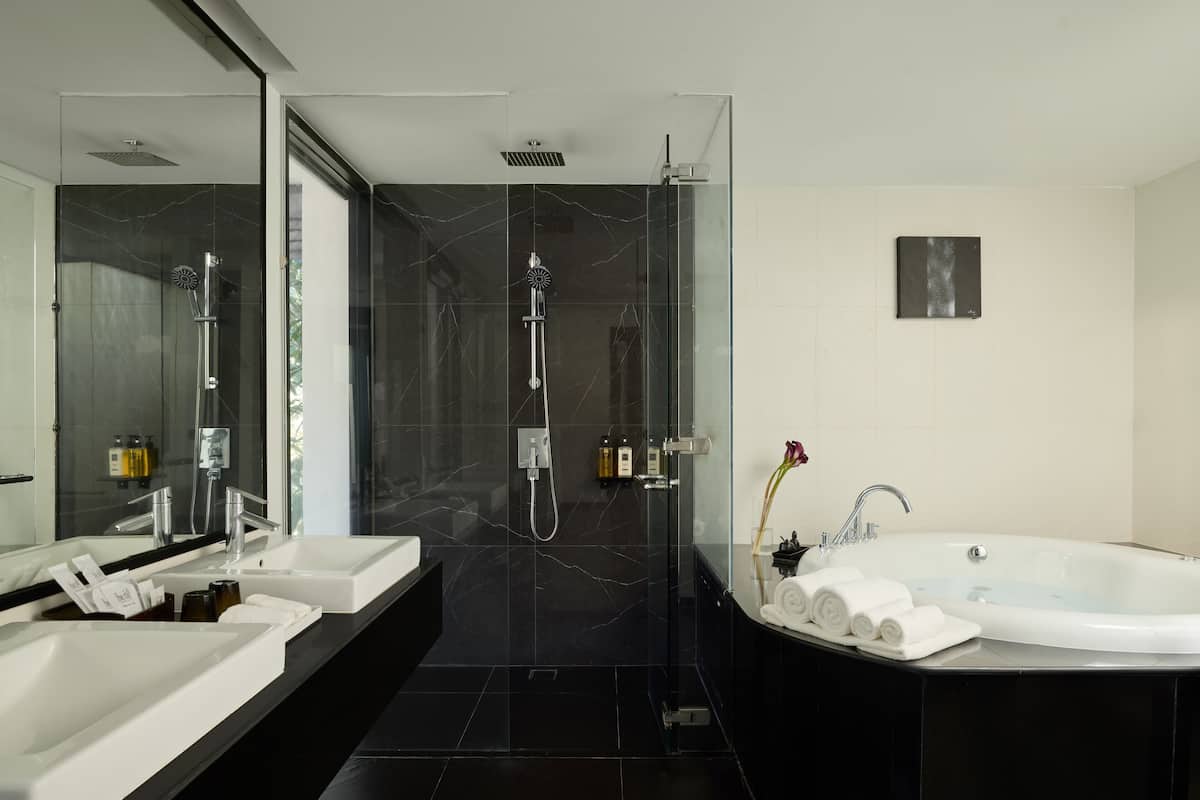 Un baño moderno con ducha envuelta en vidrio, una bañera grande e inodoros dobles.