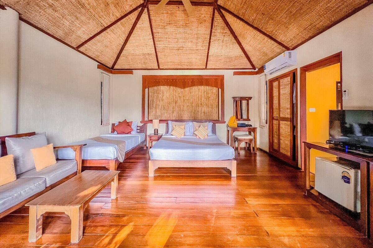 A room with a wooden ceiling, a bed, a sofa, a TV, and a small table.