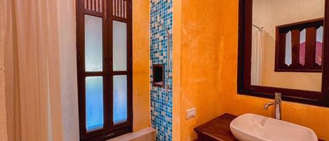Un baño con puerta de madera, zona de ducha con azulejos y un lavabo blanco con espejo.