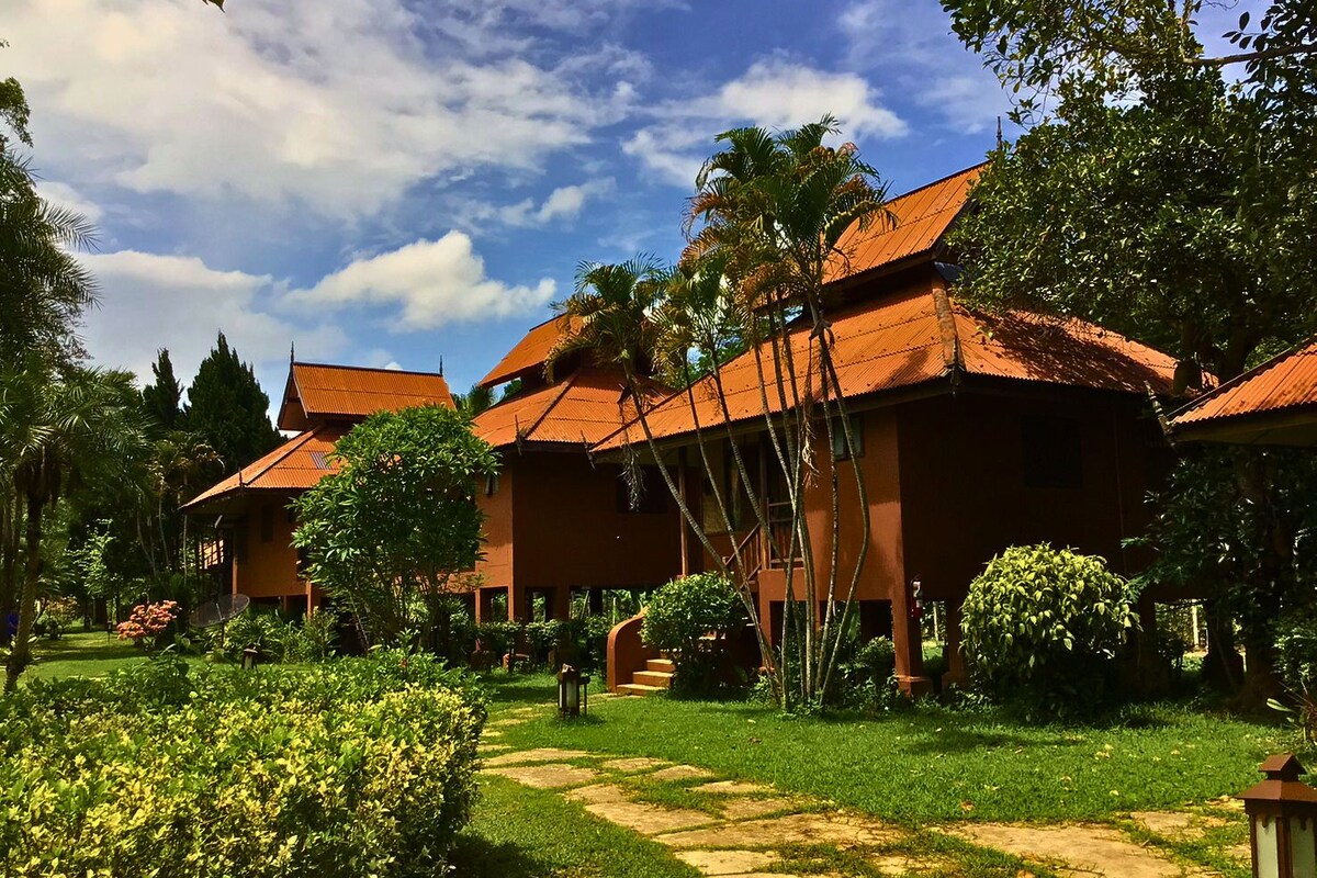 A traditional-style building with multiple rooms, surrounded by lush greenery and a clear sky.