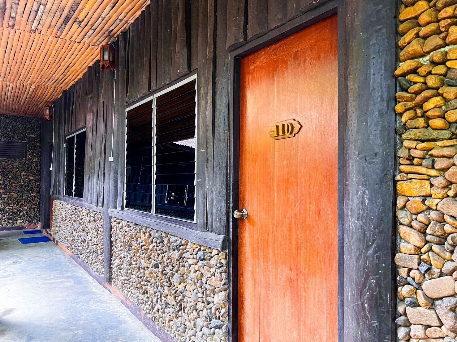A wooden building with a stone wall and a wooden door marked with the number 110.