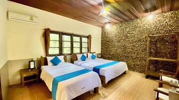 Una habitación con dos camas, una pared de piedra, techo de madera y una pequeña mesa con botellas.