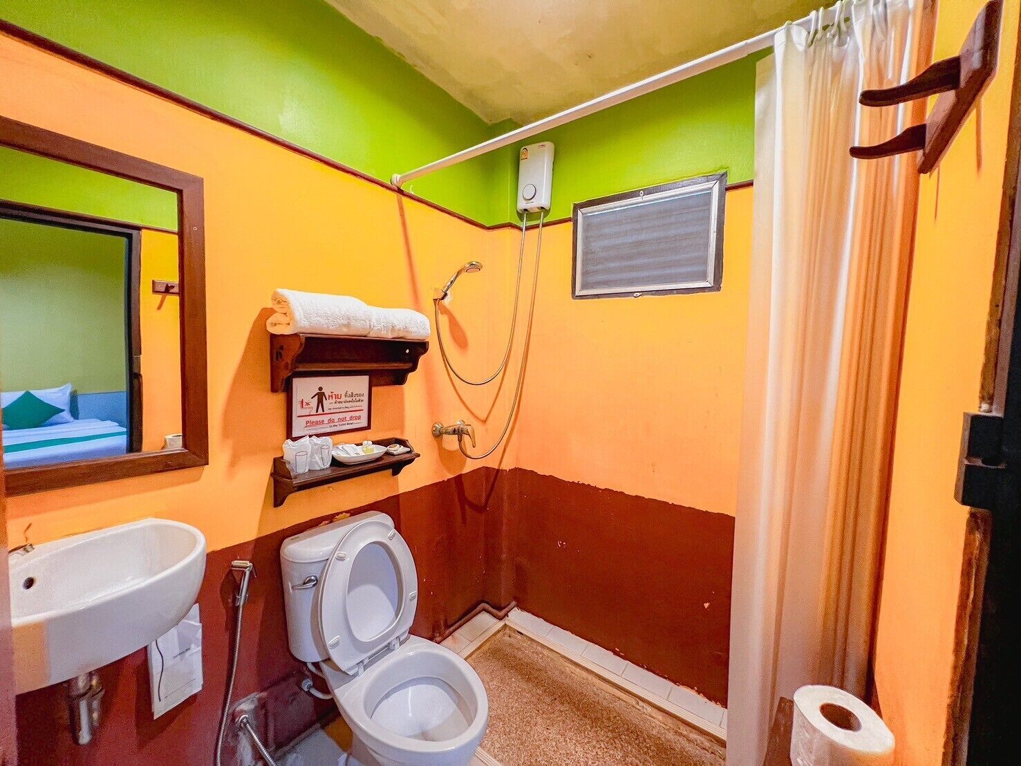 A small bathroom with a toilet, sink, and shower. There is a towel rack with a towel on it, and a sign on the wall.