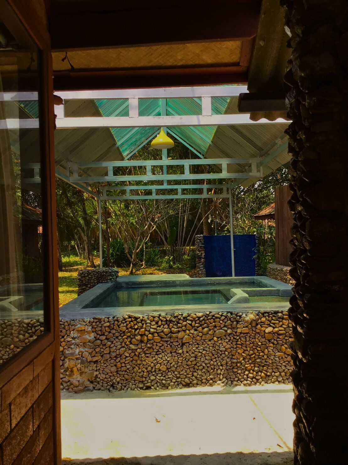 A pool area with a stone wall, a pergola, and a view of the surrounding greenery.