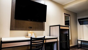 A compact kitchen with a flat-screen TV, a refrigerator, a microwave, and a wooden dining table with a chair. - Whitman Motor Lodge (Huntington Station)