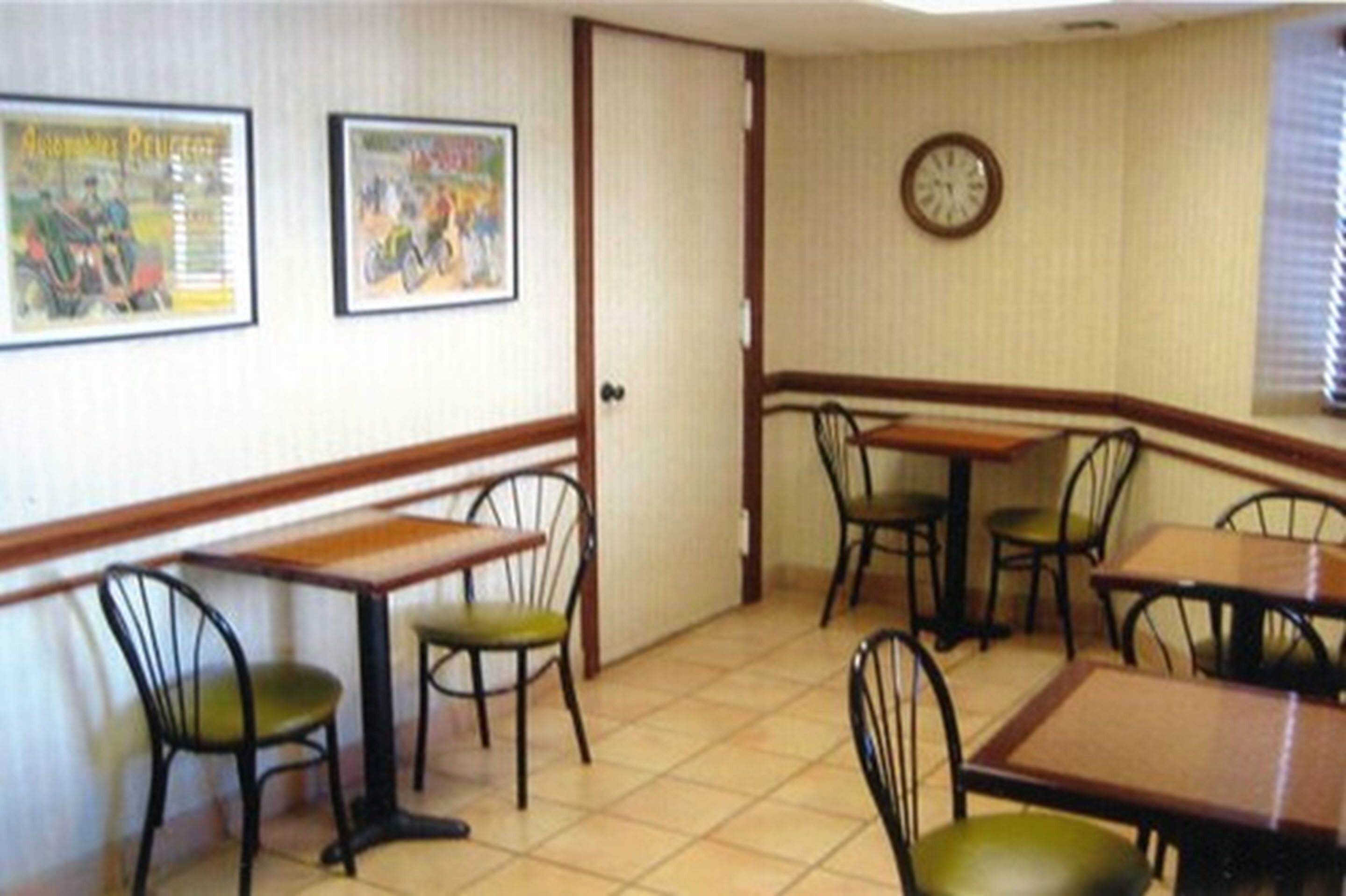Un comedor con mesas y sillas, un reloj en la pared y cuadros enmarcados.