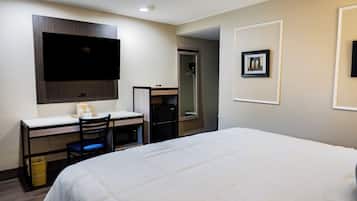 Habitación de hotel con cama, escritorio con silla, televisor montado en la pared y un cuadro enmarcado.