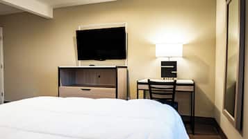 Quarto de hotel com uma cama, uma escrivaninha com cadeira, uma televisão e uma luminária.