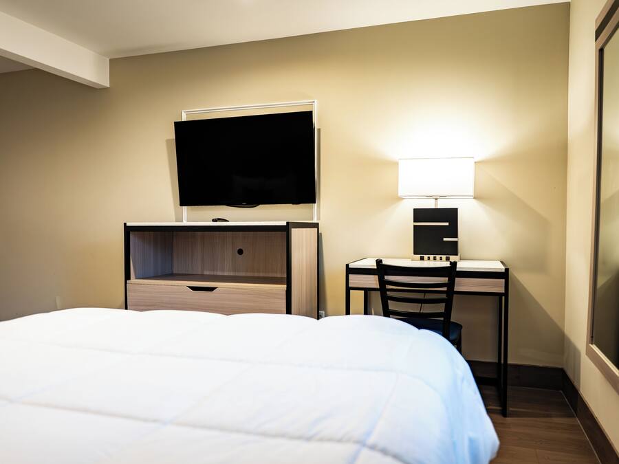 Habitación de hotel con cama, escritorio con silla, televisor y lámpara.