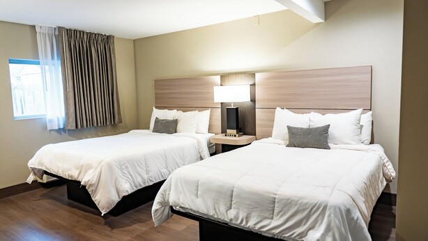 Two twin beds with white bedding, wooden headboards, bedside tables with lamps, and a window with curtains. - Whitman Motor Lodge (Huntington Station)