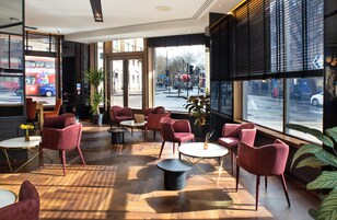 A modern interior with wooden flooring, red chairs, and round tables.