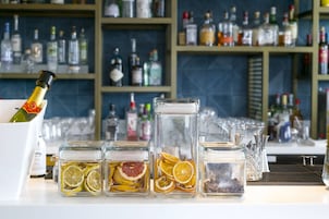 En bardisk med hyllor fulla av spritflaskor, en flaska champagne och flera glasburkar med torkade citronskivor.