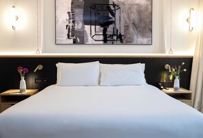Ein Hotelzimmer mit einem großen Bett, zwei Nachttischen, einem an der Wand hängenden abstrakten Gemälde und modernen Wandleuchten.