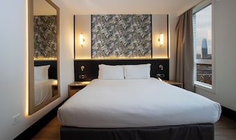 A modern hotel room with a large bed, two bedside tables, a mirror, and a city view.