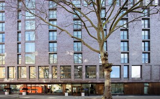 Ein modernes Hotelgebäude mit Backsteinfassade, großen Fenstern und einem Baum davor.