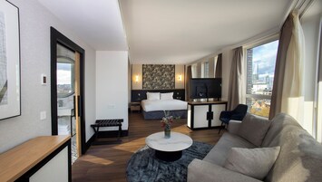 Habitación de hotel moderna con cama, escritorio, sofá y vistas de la ciudad.