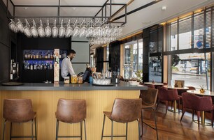 A bar area with a bartender, a wine glass rack, and a variety of bottles.