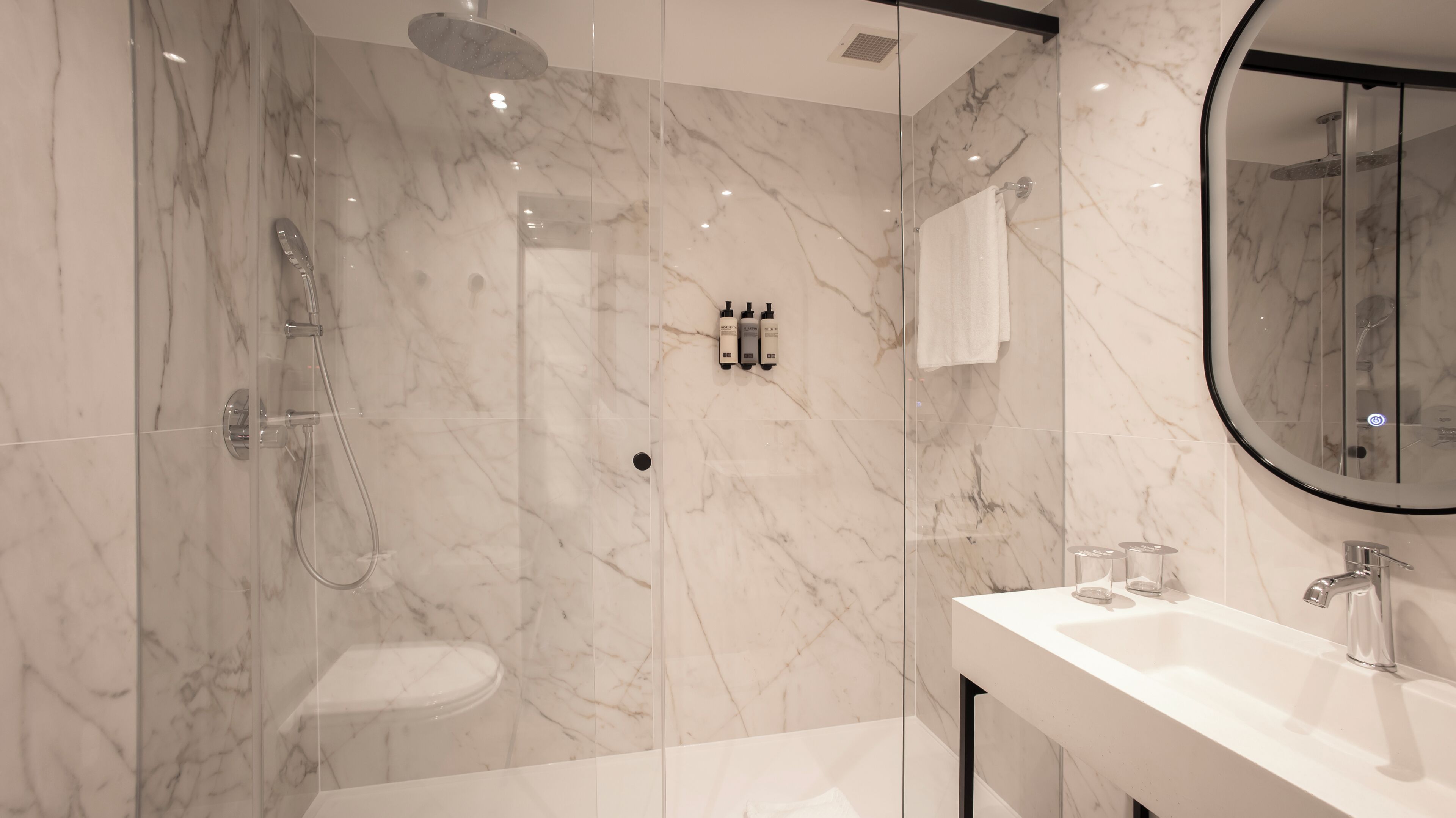 Un baño moderno con ducha de vidrio, inodoro y lavamanos con espejo.
