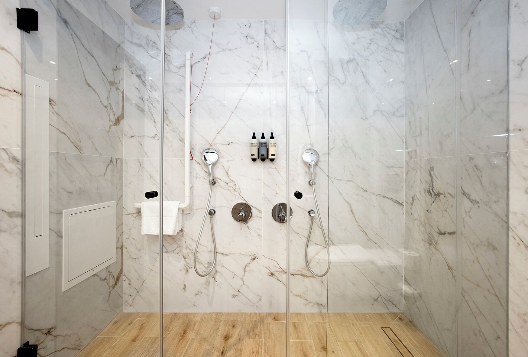 Une douche moderne avec un pare-douche en verre, des murs en marbre et un plancher en bois.