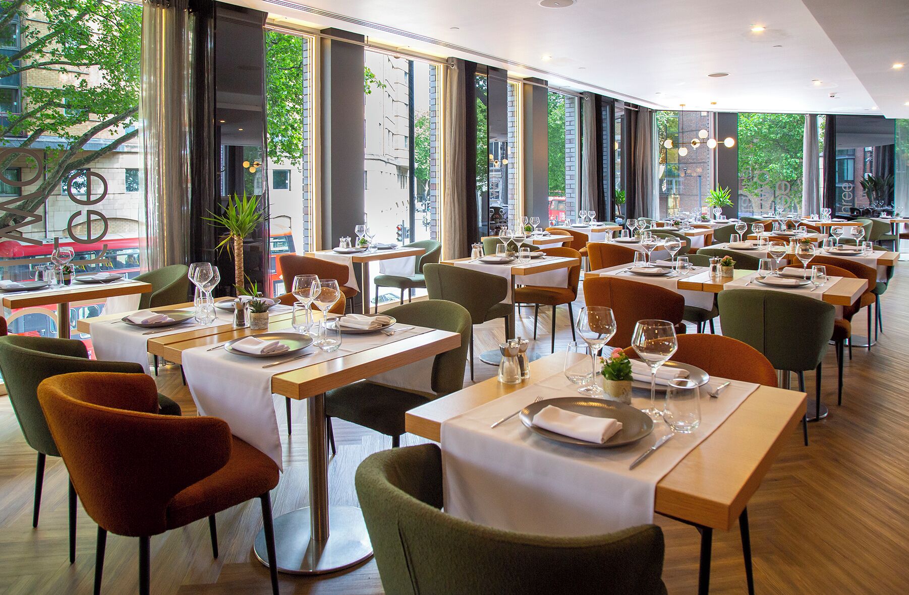 Un restaurante con varias mesas, sillas y ventanas amplias que dan a la calle.