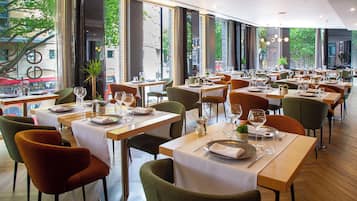 Un restaurante con varias mesas, sillas y ventanas amplias que dan a la calle.