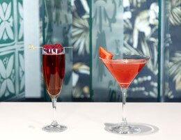 Two cocktails in martini glasses with garnishes, placed on a white surface with a decorative background.