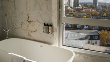 Un baño moderno con una bañera independiente, paredes de mármol y un ventanal con vista a la ciudad.