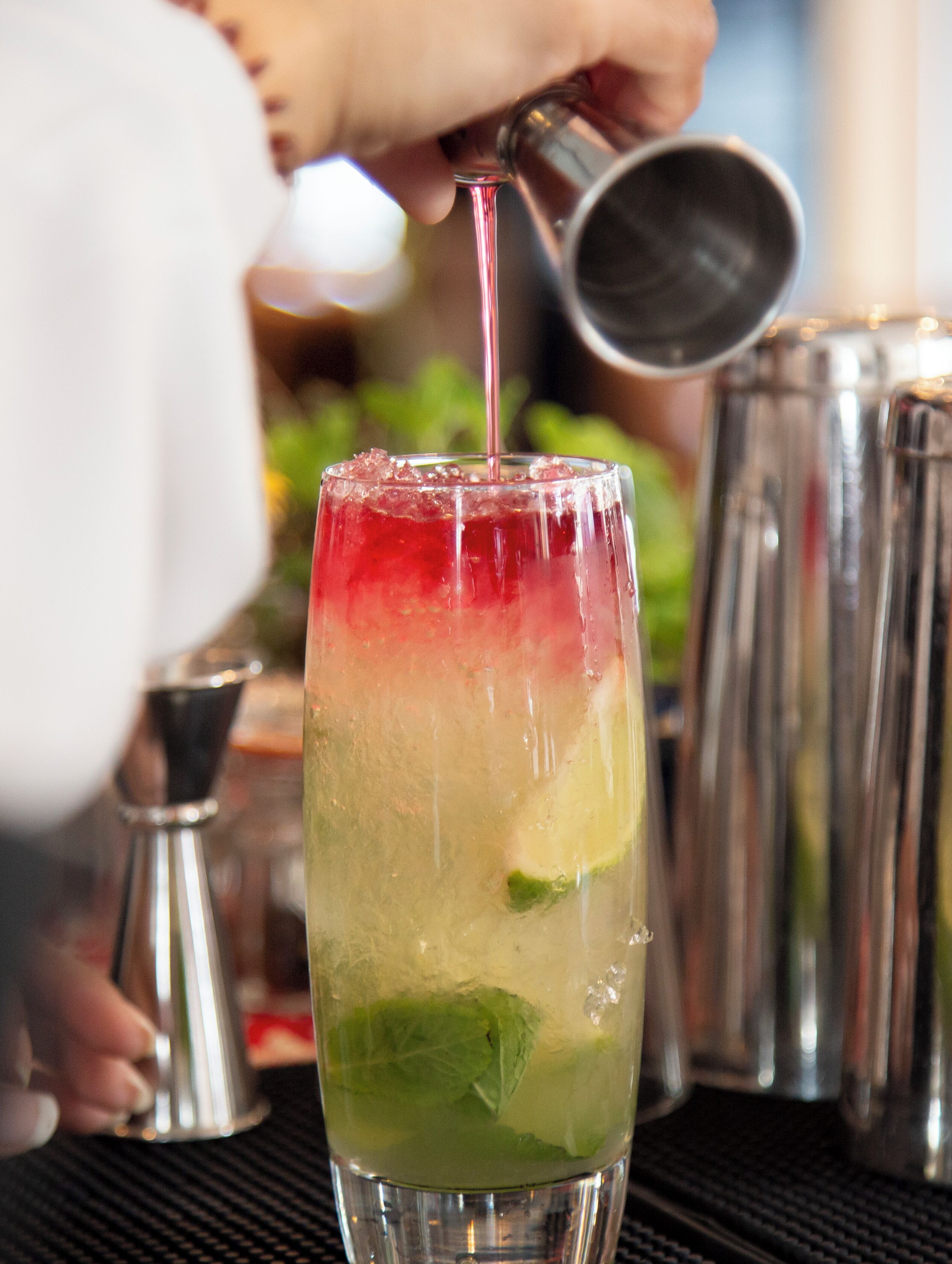 A cocktail being poured into a glass with a layered drink.