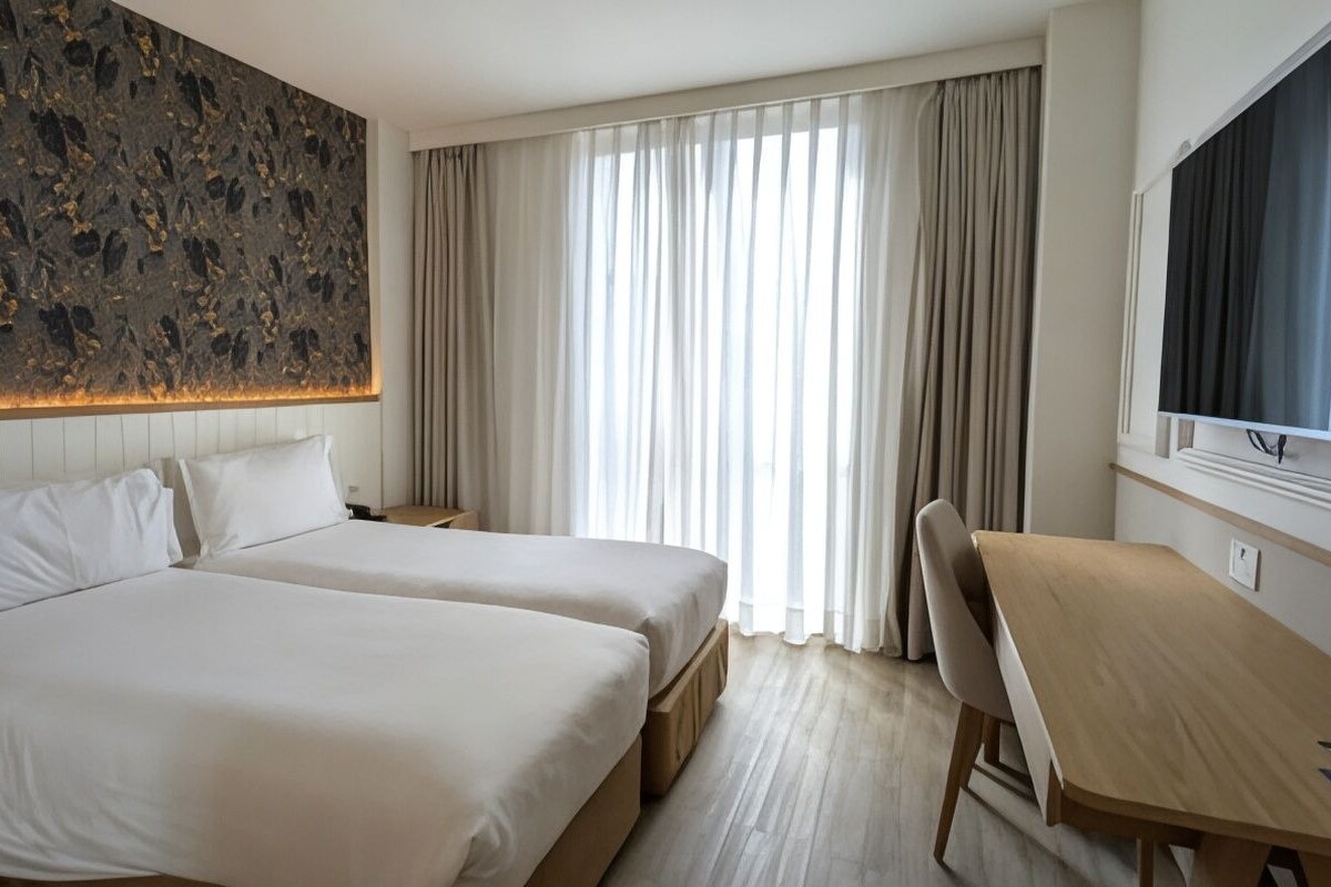 Habitació d'hotel amb dos llits, escriptori, televisió i una finestra gran amb cortines.