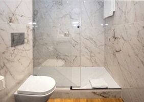 A modern bathroom with a glass-enclosed shower, marble walls, and a toilet.