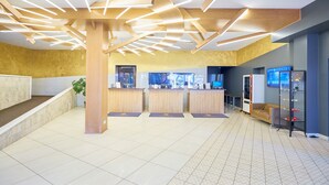 A modern reception area with a wooden reception desk, a seating area, and a digital information screen. - Hotel Dzingel (Tallinn)