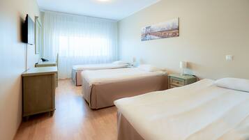 A hotel room with three beds, a desk, a chair, a TV, and a painting on the wall.