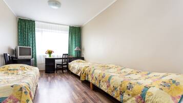 Ein Zimmer mit zwei Betten, einem Schreibtisch, einem Stuhl, einem Fernseher und einem Fenster mit Vorhängen.