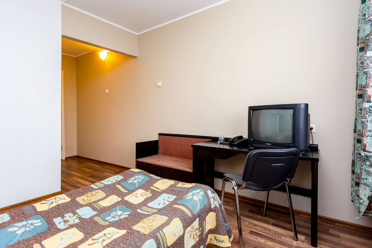 Ein Hotelzimmer mit einem Bett, einem Schreibtisch mit Computer und Telefon, einem Sessel und einem gemusterten Teppich.