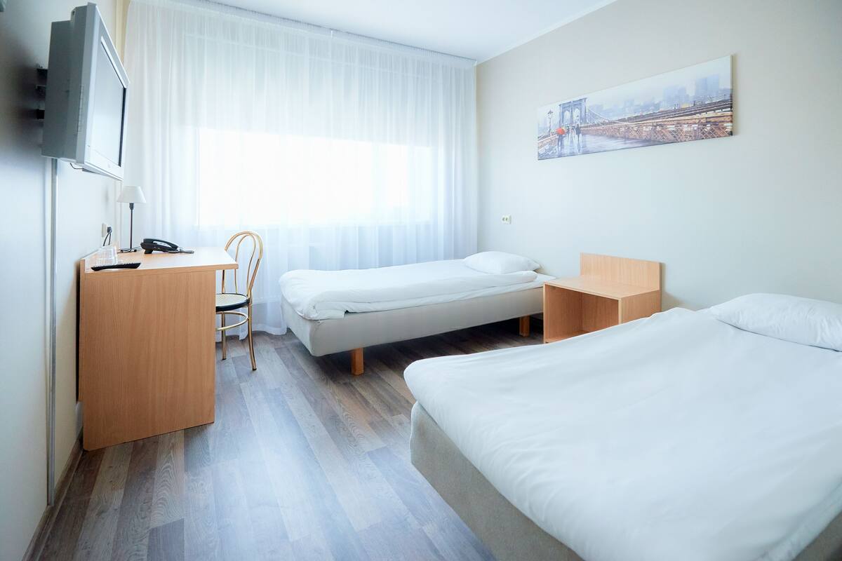 A hotel room with a bed, a desk with a computer, a chair, and a TV.