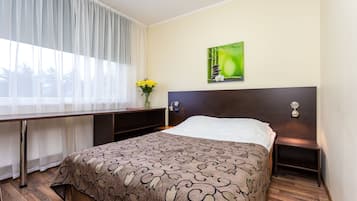 A hotel room with a bed, a desk, a chair, a nightstand, a lamp, and a painting on the wall.