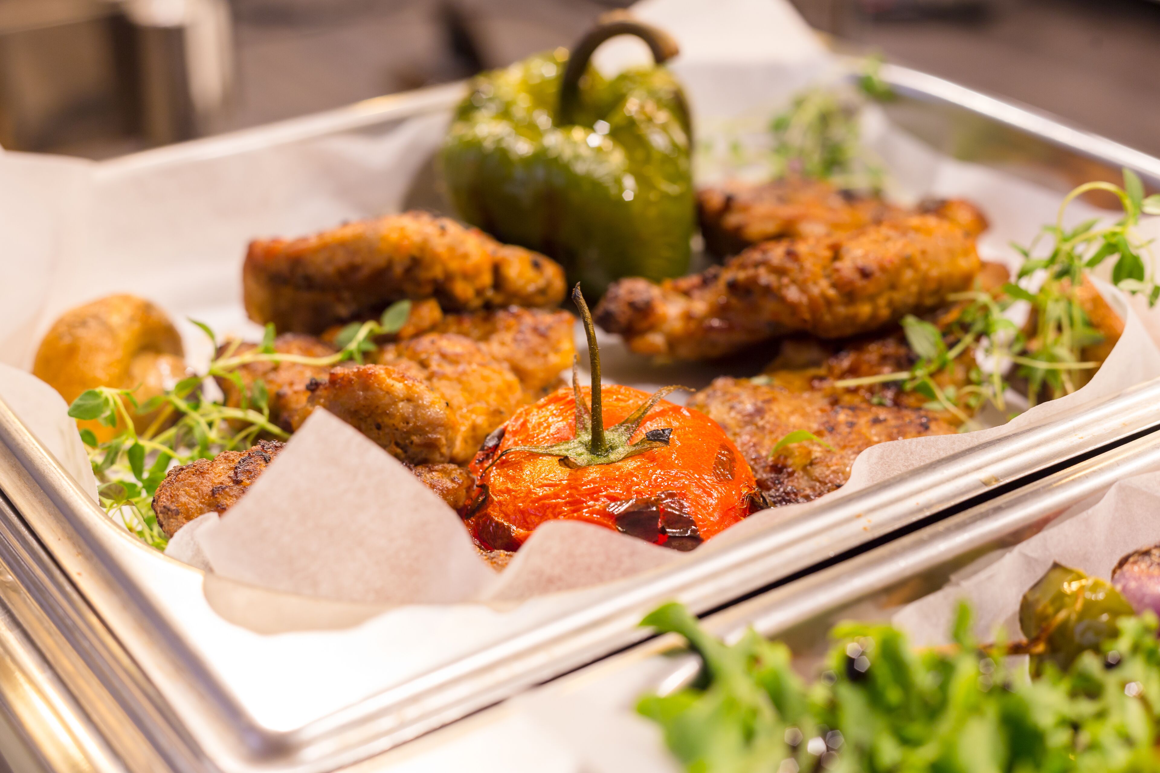 A tray of food including grilled chicken wings, a grilled tomato, and a green bell pepper.