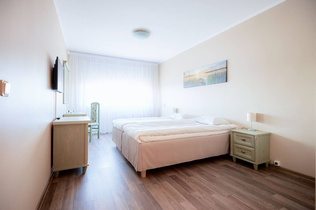 A bedroom with a bed, bedside table, lamp, and a painting on the wall.