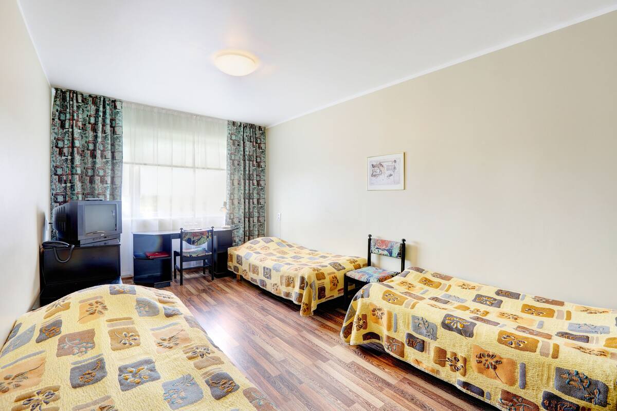 A hotel room with two beds, a desk, a chair, a television, and a window with curtains.