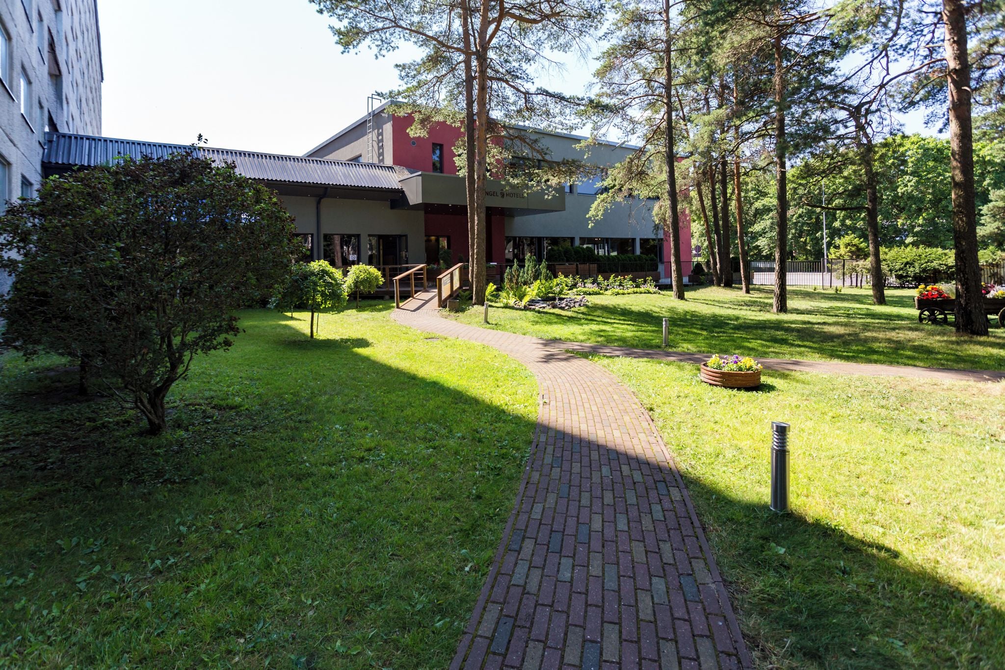 A pathway leading to a building with a red brick entrance, surrounded by greenery and trees.