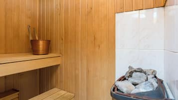 Eine Sauna mit Holzwänden, einer Holzbank, einem Kupferkübel mit Holzstäben und einem Tablett voller Steine.