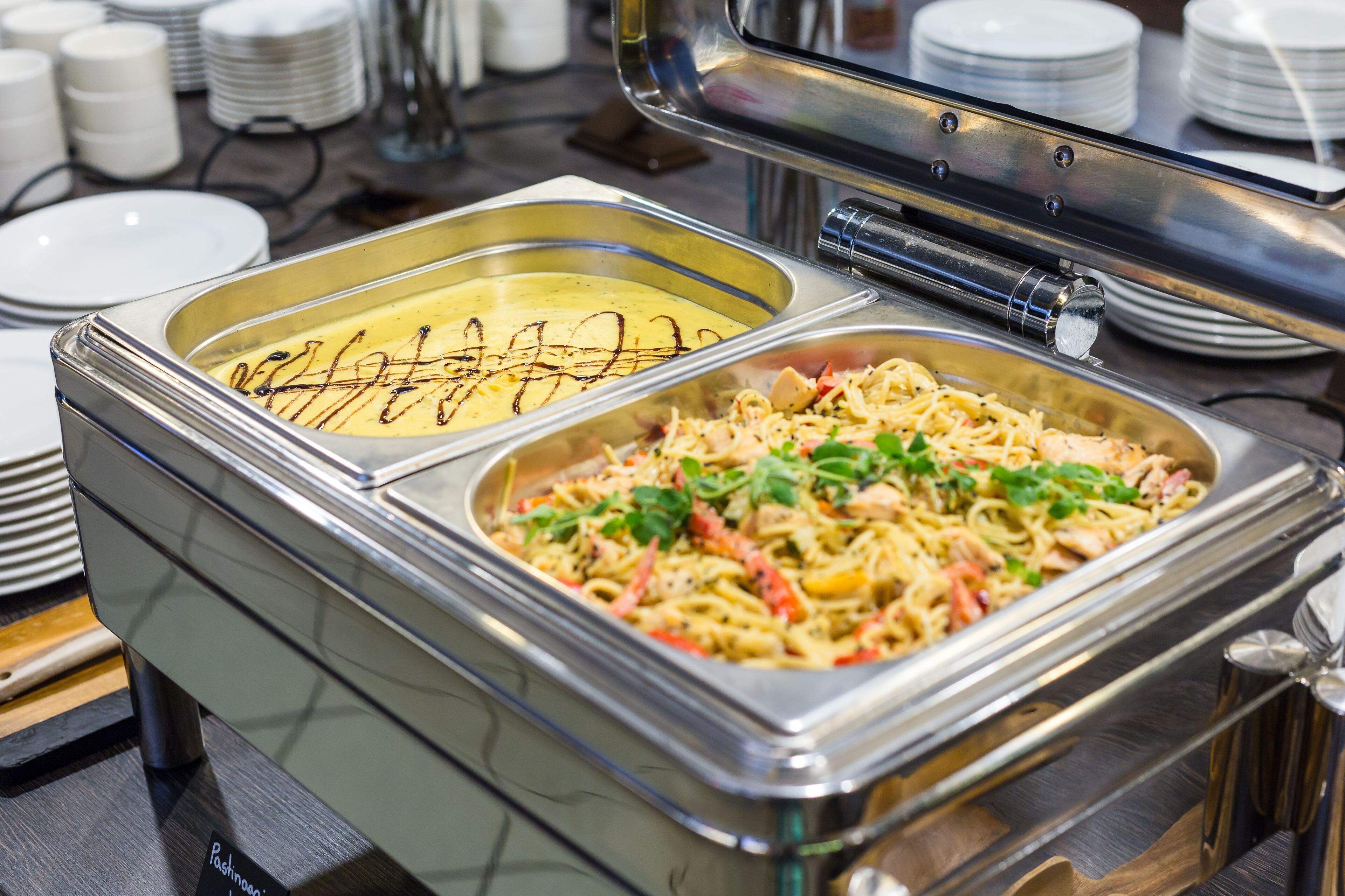 Ein Buffetsystem mit Pasta und einem cremigen Gericht, umgeben von gestapelten Tellern und Schüsseln.