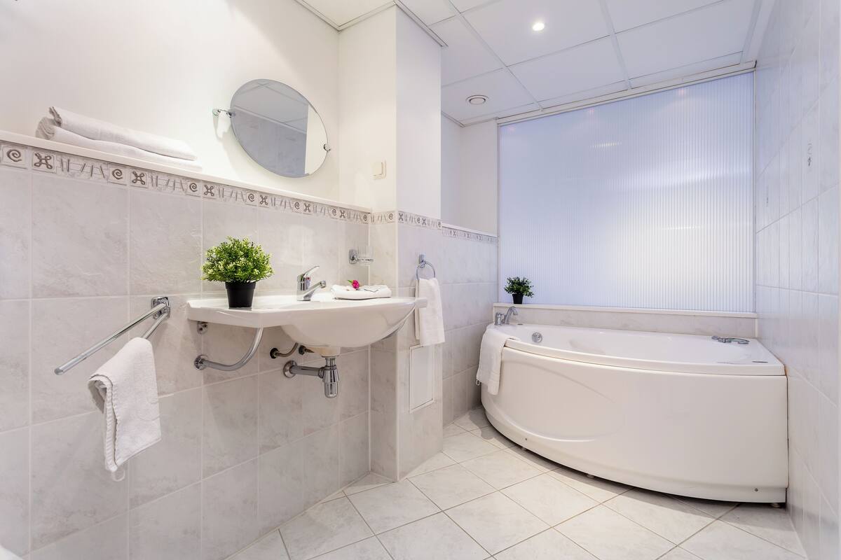 A modern bathroom with a bathtub, a sink, a mirror, and a potted plant.