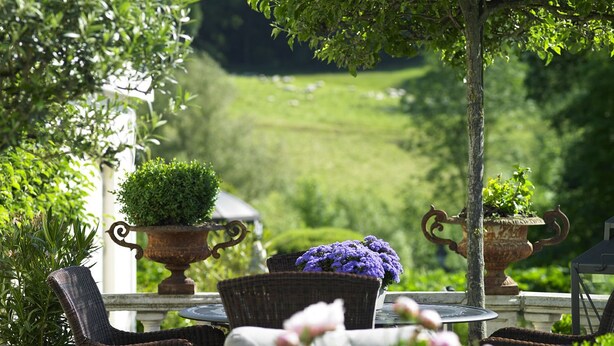 Een terras met rieten stoelen, potplanten en uitzicht op een groen landschap.