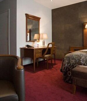 Een hotelkamer met een bureau, stoel en een bed met een bloemenprint deken.