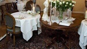 Een eetgedeelte met ronde tafels voor vier personen, witte tafelkleden, kaarsen en bloemstukken.